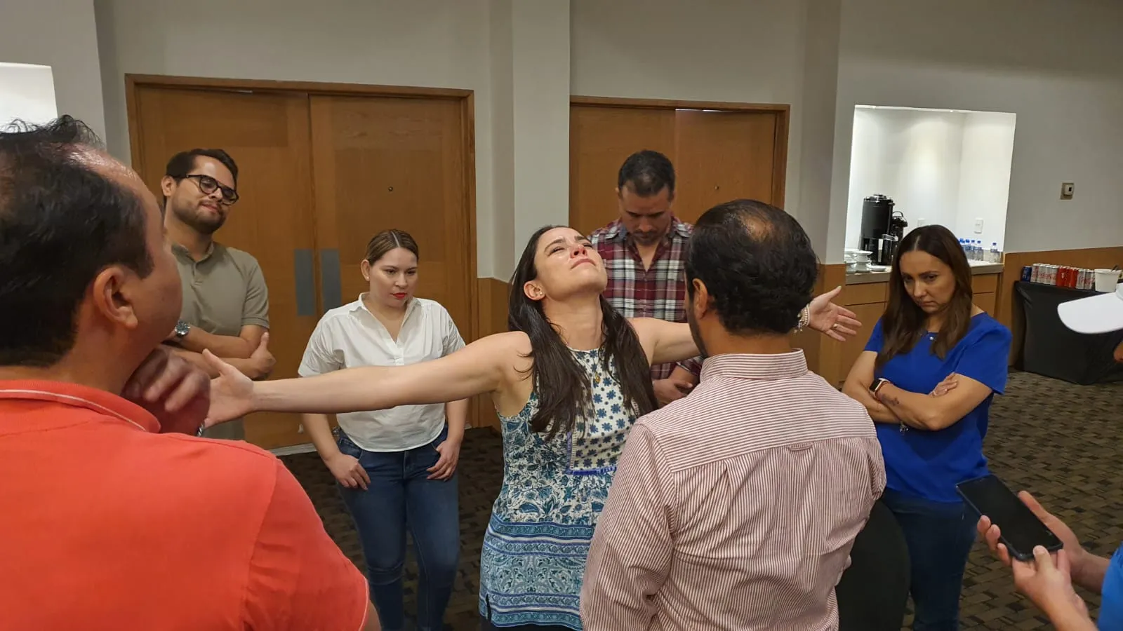 Ejemplo de una de las actividades presenciales de las dinámicas de integración laboral de Equipo Impacta. Dinámicas de integración laboral: Fotografía de mujer extendiendo los brazos rodeada de compañeros de trabajo.