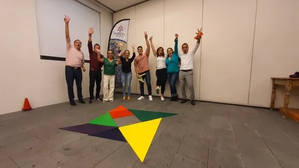 Un grupo de personas en un salón corporativo celebra con los brazos en alto después de completar uno de los juegos de trabajo en equipo para empresas.