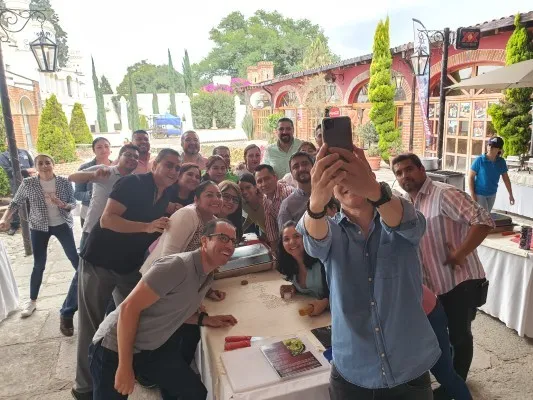 Personal de empresa junto a un compañero que sostiene un celular para comunicarse con habilidades digitales con sus colegas.