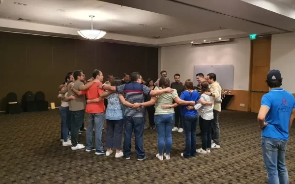 Colaboradores de una empresa formando un círculo y abrazándose en un salón como parte de dinámicas de mindfulness.