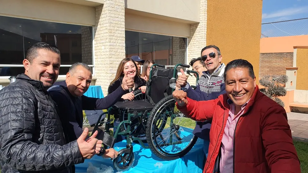 Equipo de trabajo alrededor de una silla de ruedas que construyeron juntos al aire libre para fortalecer la cohesión.