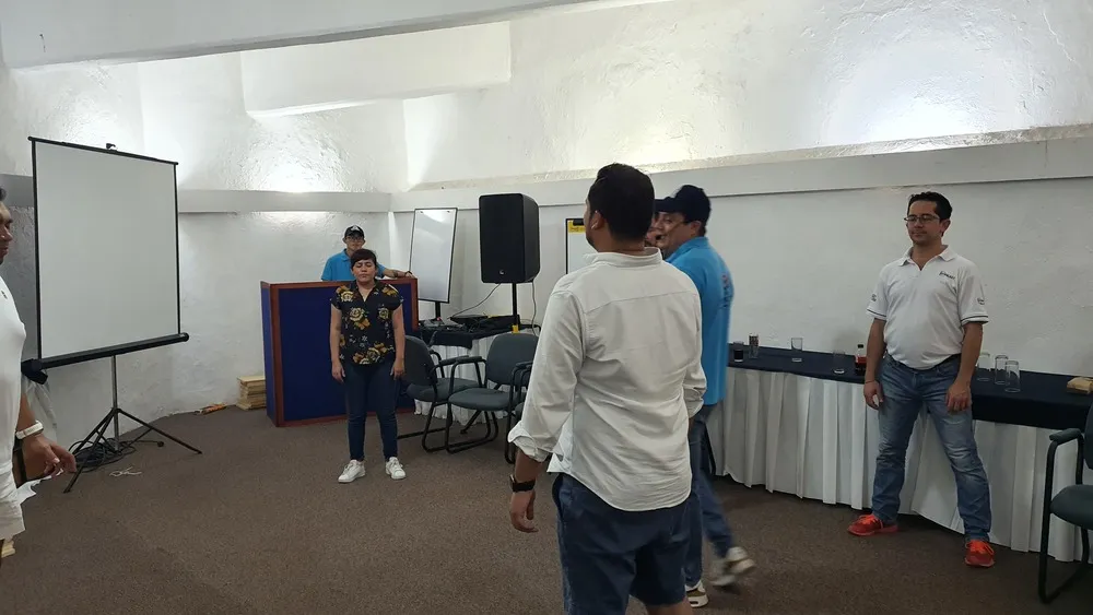 Personas de pie reunidas frente a un pizarrón blanco escuchando frases de un líder a su equipo de trabajo.