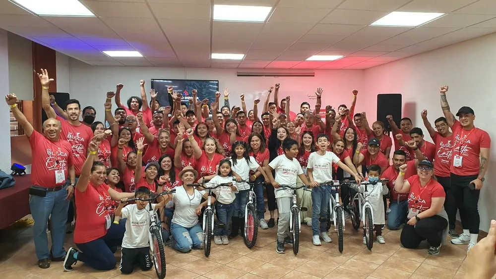 Grupo grande personas con playeras rojas de pie o en silla de ruedas realizando dinámica team building.