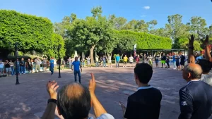 Grupo grande de personas al aire libre formando un círculo escuchando frases de un líder a su equipo.