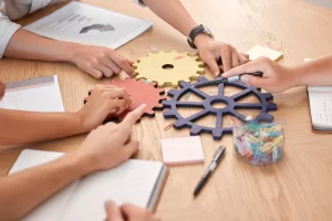 Personas señalando engranajes sobre una mesa que significa que todo funciona con ayuda de fortalezas de un equipo de trabajo.