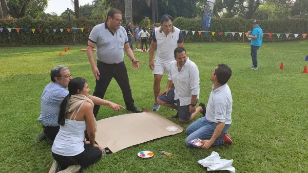 Fotografía de colaboradores de pie alrededor de un papel color café durante actividad para el manejo de las emociones.