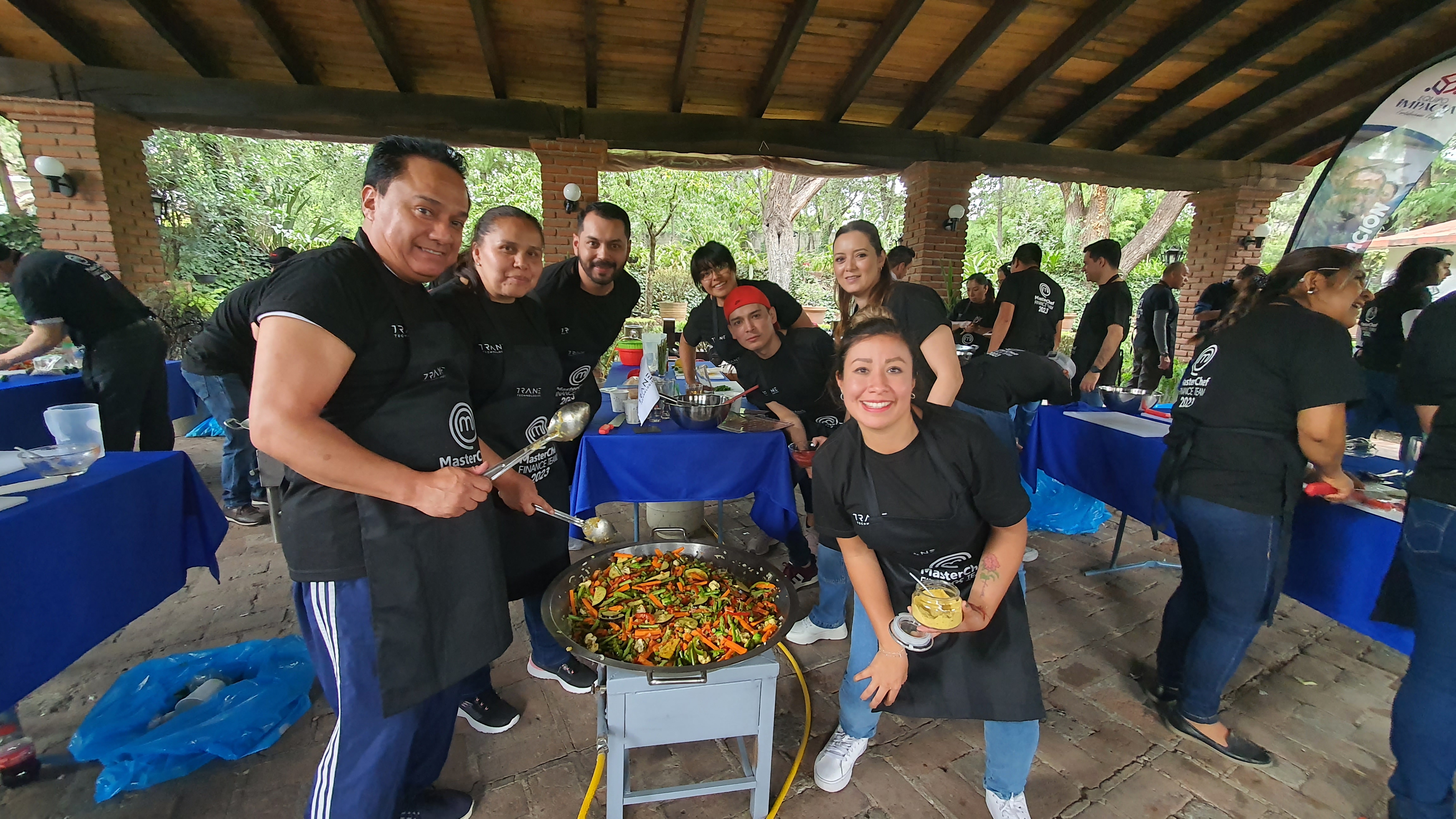 Fotografía de un equipo de trabajo de una empresa usando mandiles a lado de una cacerola durante la dinámica master chefs.