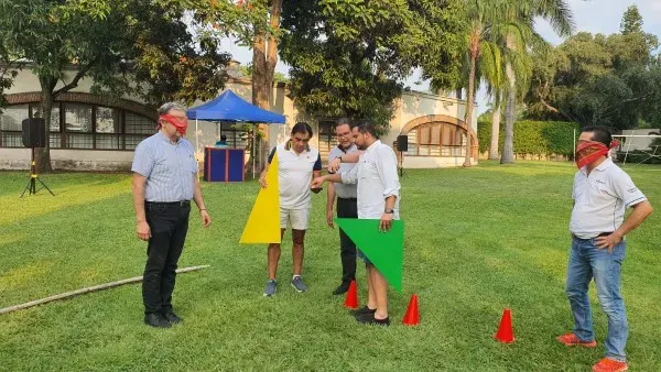 Ejemplo de una dinámica presencial que se lleva a cabo con el equipo de trabajo de una empresa para mejorar la cohesión. Fotografía de colaboradores reunidos al aire libre durante dinámica presencial que se realiza con figuras de colores.