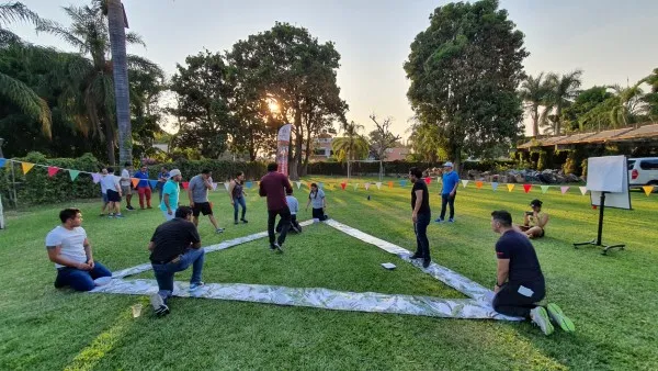 Team building Querétaro que promueve una comunicación interna eficiente para fortalecer la confianza y la cohesión. Team building Querétaro: Fotografía de colaboradores colocados en los puntos de un triángulo que está en el pasto.