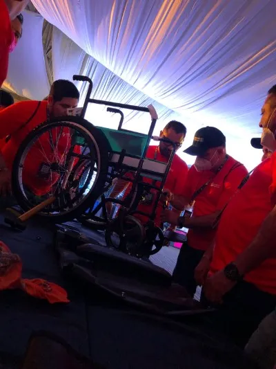 Ejemplo de actividad de team building Querétaro que lleva a cabo Equipo Impacta: Construyendo una silla de ruedas. Team building Querétaro: Fotografía de personas utilizando playeras color rojo mientras arman una silla de ruedas.
