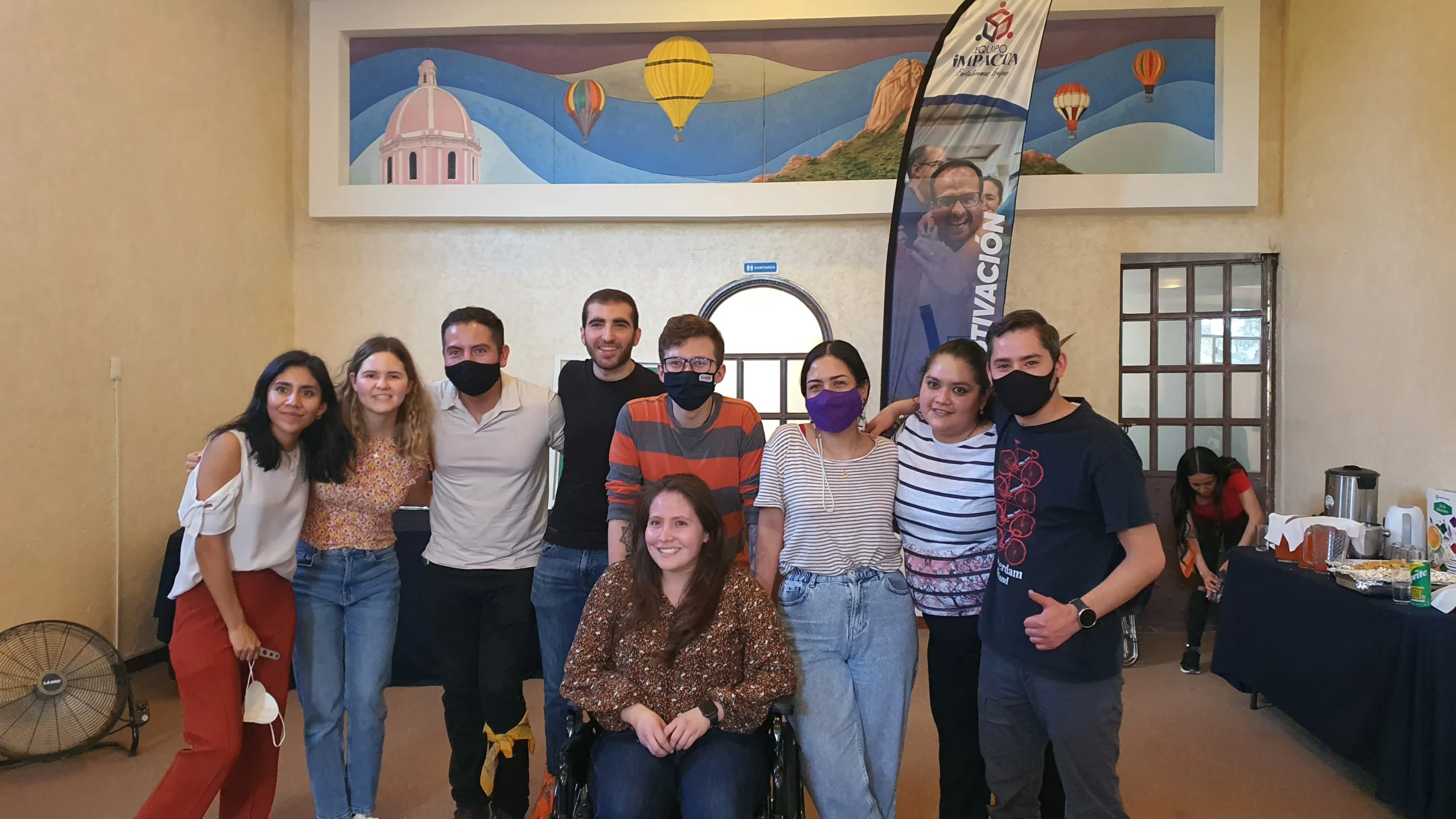 Integración empresarial para fomentar la participación de todos los colaboradores y lograr los objetivos. Integración empresarial: Fotografía de un grupo de personas en un salón y a lado una mesa con mantel color azul marino.